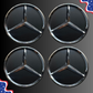 Four Mercedes-Benz three-pointed star emblems arranged in a 2x2 grid on a dark gray background, with small decorative American flag graphics in the top-right and bottom-left corners.